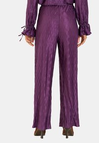 Fioletowe satynowe spodnie w szerokim kroju o falistym wzorze, z elastycznym pasem i troczkami przy mankietach. Skrojone na luźny fason.