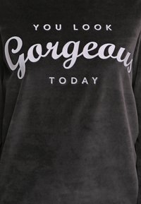 Sudadera gris oscuro hecha de un tejido suave con letras blancas que dicen: "HOY TE VES HERMOSA" en diferentes estilos de fuente.