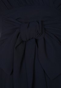 Abito blu navy con corpino arricciato e ampia cintura in tessuto annodata a fiocco, realizzato in un tessuto morbido e testurizzato, con dettagli di drappeggio a strati.