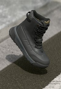 Czarne wodoodporne buty z teksturowaną cholewką, wzmocnionym noskiem, sznurowanym designem i grubą gumową podeszwą z wzorzystym bieżnikiem.