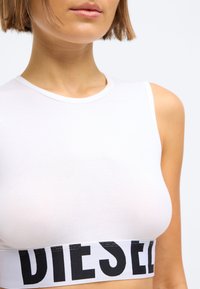 Λευκό αμάνικο crop top με στρογγυλή λαιμόκοψη και μαύρη λωρίδα λογότυπου "DIESEL" στο τελείωμα, με απαλή, εφαρμοστή σχεδίαση.