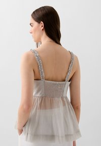 Top peplum grigio chiaro con corpetto arricciato e spalline con volant, caratterizzato da una texture a strati in tessuto trasparente. Visibile la vista posteriore.