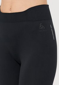 Black high-waisted leggings made from stretchy knit fabric, featuring a smooth texture, logo detail, and subtle performance print on the side.