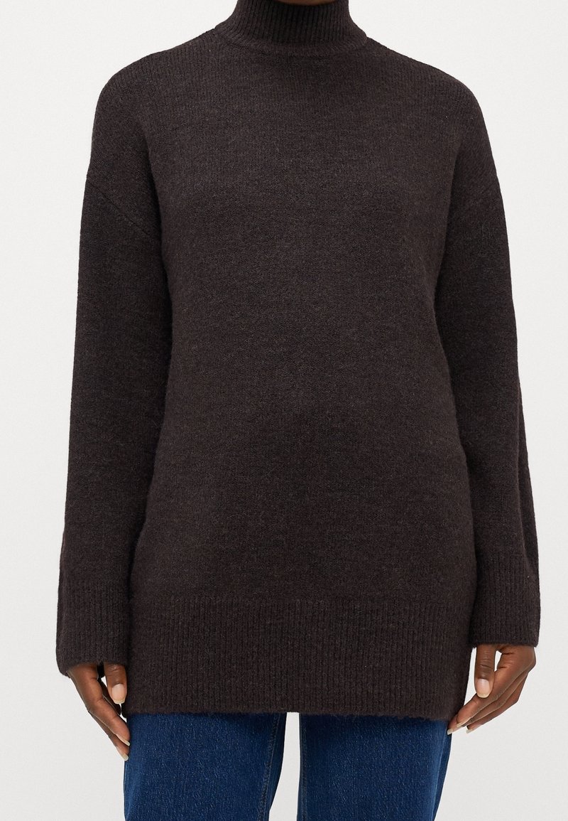 Dunkelbrauner, gestrickter Langarmrollkragenpullover, getragen über blauen Jeans, an einer Person mit dunkler Haut.