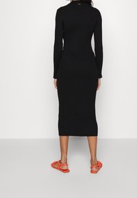 Černé žebrované midi šaty s dlouhými rukávy, přiléhavým střihem a bočním rozparkem. V kombinaci s jasně oranžovými plochými sandály.