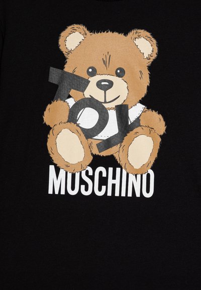Camiseta negra con un oso de peluche de dibujos animados con pelaje marrón y ojos negros, sosteniendo un letrero gris que dice "Toy", con "MUSCHINO" impreso debajo en blanco.
