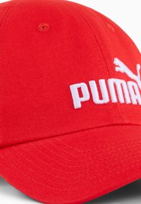 Czerwona czapka z bawełny z wygiętym daszkiem, zdobiona białym haftowanym logo i ozdobnym przeszyciem na powierzchni.