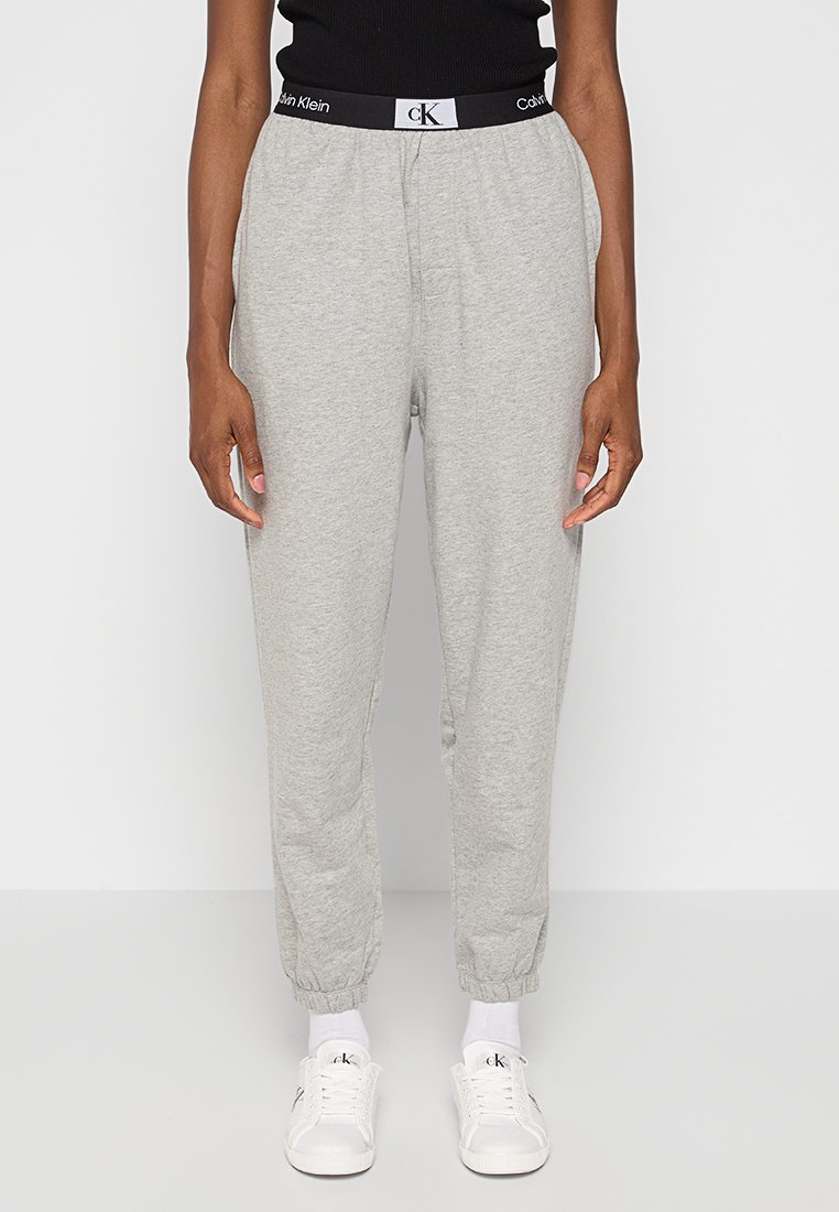 Pantaloni sportivi grigi con vita elastica, dotati di logo Calvin Klein in bianco e nero. Caviglie a polsino, materiale morbido e design affusolato.
