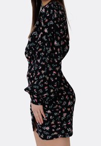 Svart blommig klänning med långa ärmar, en figurnära silhuett och en sidoklyvning. Tyget visar små rosa och gröna blommönster.