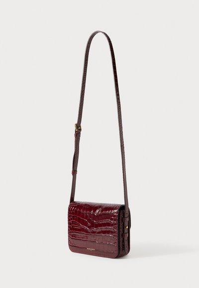Γυαλιστερό σταυρωτό τσαντάκι από σκλήρυντο δέρμα σε σκούρο κόκκινο με ανάγλυφη υφή κροκοδείλου, ρυθμιζόμενο λουράκι και χρυσό λογότυπο στην μπροστινή πτερύγια.
