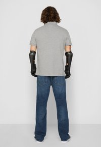 Grå poloskjorte med korte ermer, kombinert med blå denimbukser. Svart protesearmer med teksturerte overflater og fingeråpninger.