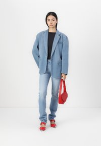 Denim blazer in svetlo modri barvi in jeans, v kombinaciji s prilegajočo črno majico. Rdeča torbica trdne oblike in rdeče čevlje s koničastim nosom z metalnimi poudarki.