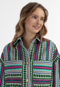 Spalvingas raštuotas švarkas su žaliai, rožine ir mėlyna juostelėmis bei auksiniais akcentais; du kišenės ir apykaklės iškirptė.