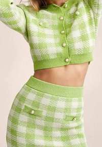 Top corto lavorato a maglia a quadri verdi e bianchi con accenti di perle, abbinato a una gonna coordinata con bottoni e tasche frontali.