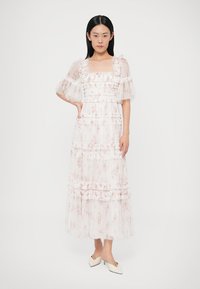 Biała sukienka maxi w kwiaty z przezroczystymi bufkami, falbanami i warstwami, zestawiona z kremowymi szpilkami na szpic.