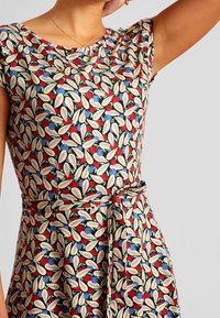 Upravené šaty s vícobarveným vzorem listů na červeném pozadí, s krátkým rukávem a detailem zavázaného pasu. Hladká textura látky.