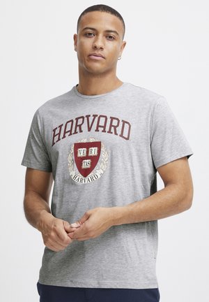 Grå t-skjorte med korte ermer som har et Harvard-logo i mørkerødt med skjold og laurbærdesign. Glatt bomullsstoff, rund hals.