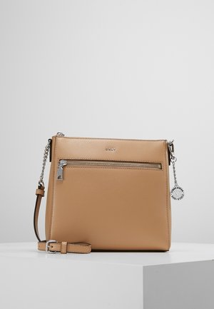 Tan leren crossbody tas met een voorvak met rits, zilveren hardware, verstelbare schouderband en logo detail. Gladde textuur en minimalistisch ontwerp.