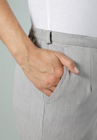 Pantaloni grigio chiaro con texture, dotati di una cintura elastica e tasche laterali. Mano appoggiata nella tasca, evidenziando la morbidezza e i dettagli del tessuto.