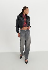 Black leather cropped jacket, burgundy floral crop top, gray wide-leg jeans, and black pointed-toe heels, standing on a neutral background.