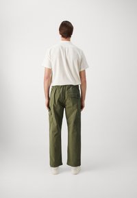 Short-sleeve white shirt with textured fabric, paired with olive green cargo pants featuring pockets, relaxed fit, and elastic waistband.