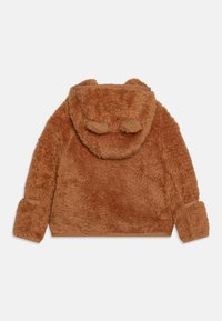 Giacca in pile marrone e morbido con cappuccio, dotata di dettagli a forma di orecchie di animale. Fodera liscia, tasche laterali e polsini elasticizzati.