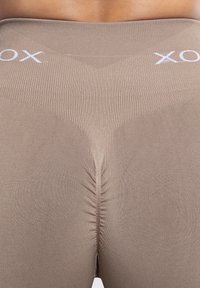 Beige legging met een rekbare, geribbelde textuur. Kenmerkt zich door een hoge tailleband met een wit logo en een geplooide naad aan de achterkant.