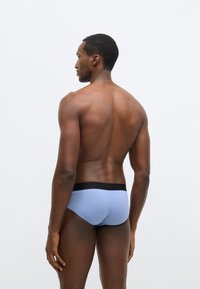 Chiloți scurți din bumbac albastru, cu talie elastică neagră, croială ajustată, textură netedă și fără modele sau accente vizibile.