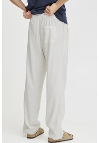 Světle béžové volné lněné kalhoty s elastickým pasem a jednou zadní kapsou. Měkká textura a volný střih pro pohodlí.