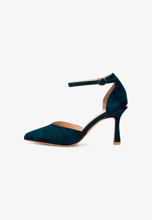 Zapato de tacón alto de gamuza en azul oscuro con puntera afilada, tira en el tobillo con un hebilla circular y una suela exterior sutilmente naranja.