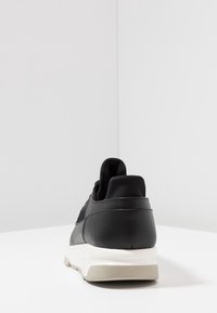 Basket en cuir noir avec un design à coupe basse, présentant un dessus texturé et une semelle intermédiaire blanche. Bout arrondi et détail de col rembourré.