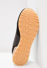 Schwarzer Sportschuh mit strukturiertem Obermaterial und einer Gummisohle, die ein geometrisches Profil in hellorange aufweist. Der Markenname "Skechers" ist sichtbar.