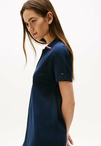 Polo de color azul marino con mangas cortas, que presenta un cuello en rojo y blanco en contraste. Incluye un pequeño logotipo en la manga izquierda. Textura suave.