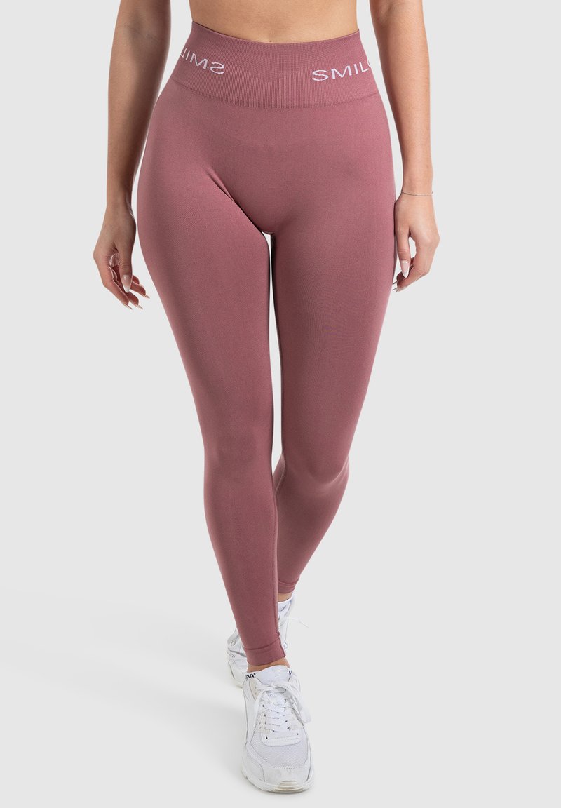 Collant rosa a vita alta con finitura testurizzata e logo "SMIL" all'altezza della vita, abbinati a scarpe da ginnastica bianche.