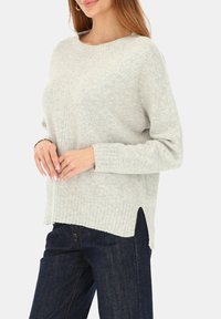 Jasnoszary sweter dzianinowy z okrągłym dekoltem, prążkowanymi mankietami i krawędzią. Posiada boczne rozcięcia i subtelny fakturowany wzór. Połączony z ciemnymi dżinsami.