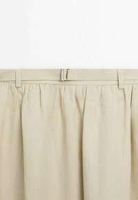 Jupe en lin beige avec un design froncé, dotée d'une ceinture tissée et d'une boucle en métal à la taille. Texture lisse, tissu léger.