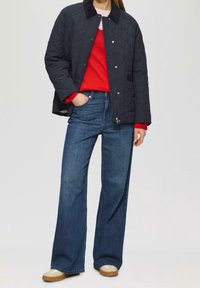 Granatowa pikowana kurtka z kołnierzem, pod spodem czerwony sweter oraz szerokie niebieskie jeansy. Kurtka posiada zamek błyskawiczny i zatrzaski, ma luźny krój.