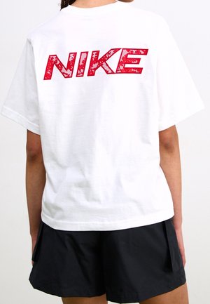 Personne portant un t-shirt Nike blanc avec un logo rouge dans le dos et un short noir, debout de dos face au spectateur.