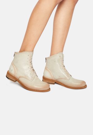 Bottines en beige perforé à lacets sur le devant, avec une semelle en bois et des détails lisses à la cheville. Comprend une fermeture éclair sur le côté pour un enfilage facile.