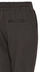 Pantalon marron foncé à motif chevrons avec taille élastique et une seule poche passepoilée à l’arrière droit.