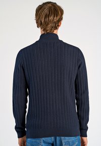 Dunkelblauer, gerippter Pullover mit hohem Kragen, gestrickter Textur und langen Ärmeln. Auffällig ist das vertikale Muster und die taillierten Bündchen.