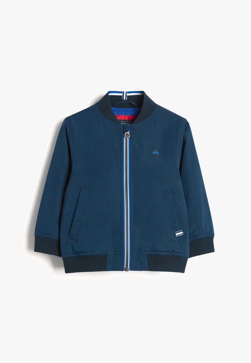 Blouson aviateur bleu marine, avec une fermeture éclair à l'avant, des poignets en maille, des poches latérales et une doublure rayée bleue et rouge. Présente un petit logo sur la poitrine.