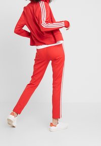 Červený teplákový komplet s bílými pruhy na rukávech a po stranách, střih zkráceného sáčka, upnuté kalhoty a v kombinaci s bílými teniskami.