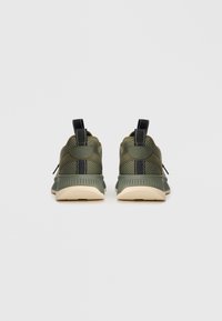 Baskets de sport vertes avec un matériau texturé, un accent noir et une semelle beige. Présentent des languettes à l'arrière pour un enfilage facile.