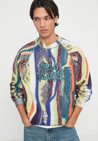 Multifarvet strikket sweatshirt med rund hals, raglanærmer og livlige mønstre i blå, grønne og røde farver samt en grafisk detalje.