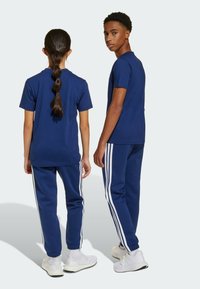 T-shirts et joggings en coton bleu marine avec des rayures blanches sur les côtés, coupe décontractée et poignets élastiques, portés par deux personnes de dos.