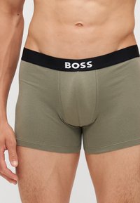 BOSS muške bokserice u maslinasto zelenoj boji, izrađene od mekog pamuka, s crnim elastičnim pojasom koji sadrži bijeli logotip.