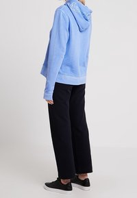 Sudadera con capucha de color azul claro con cordón y logo bordado en la capucha, combinada con pantalones anchos de color negro y zapatillas negras. Material suave.