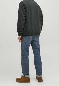 Tmavě šedá fleecová bunda s žebrovaným lemem a manžetami, doplněná modrými džínami s klasickým designem pěti kapes a ohrnutými lemy. Hnědé kožené boty.