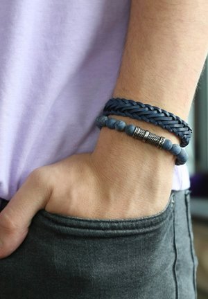 Marine leren gevlochten armband met zilveren accenten, gecombineerd met een kralenarmband met donkerblauwe stenen en zilveren details.